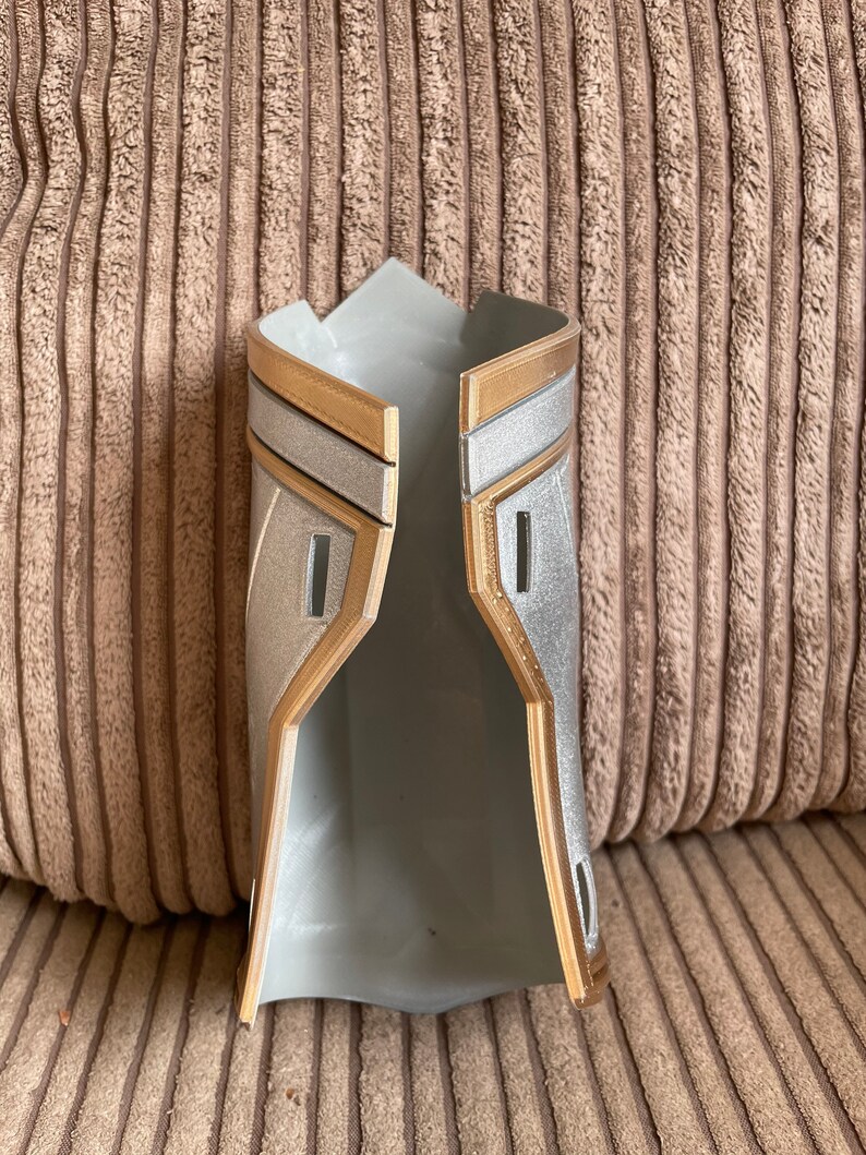 May include: A pair of silver and gold-coloured armour gauntlets, made of plastic, are open and ready to be worn.