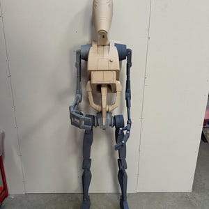 May include: A partially assembled, beige and gray plastic action figure of a robot. The robot has a humanoid shape with a large head and articulated limbs.
