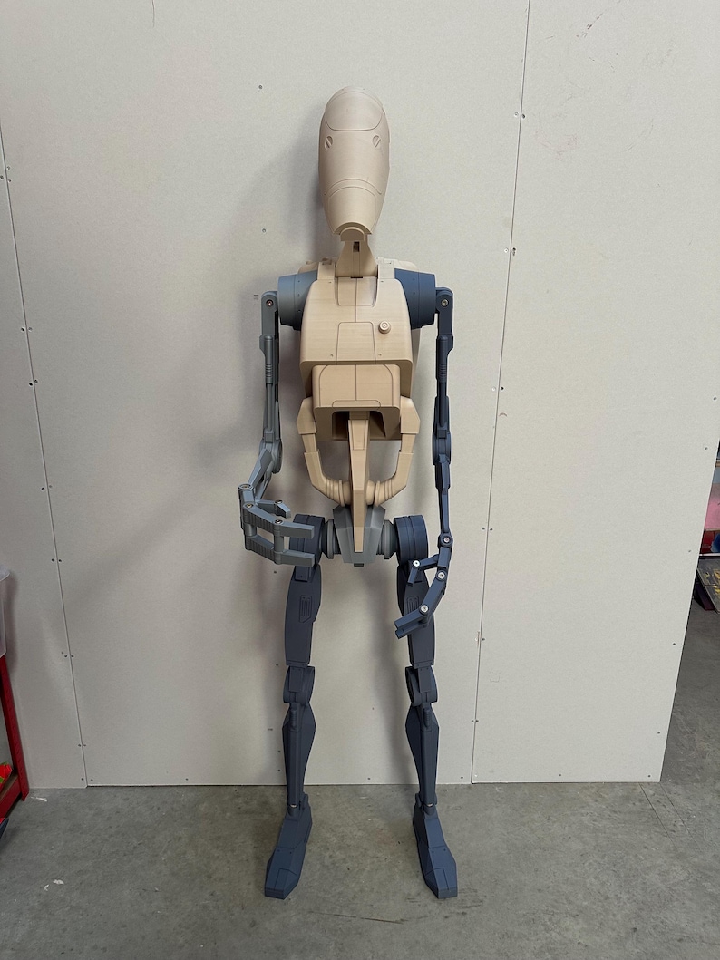 May include: A partially assembled, beige and gray plastic action figure of a robot. The robot has a humanoid shape with a large head and articulated limbs.