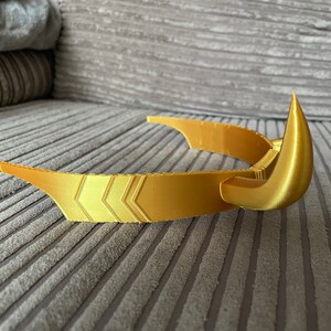 Puede incluir: Una corona dorada con un dise&ntilde;o curvo y puntas afiladas. La corona presenta patrones de chevr&oacute;n a lo largo de la banda. El dise&ntilde;o sugiere un tema de fantas&iacute;a o cosplay.