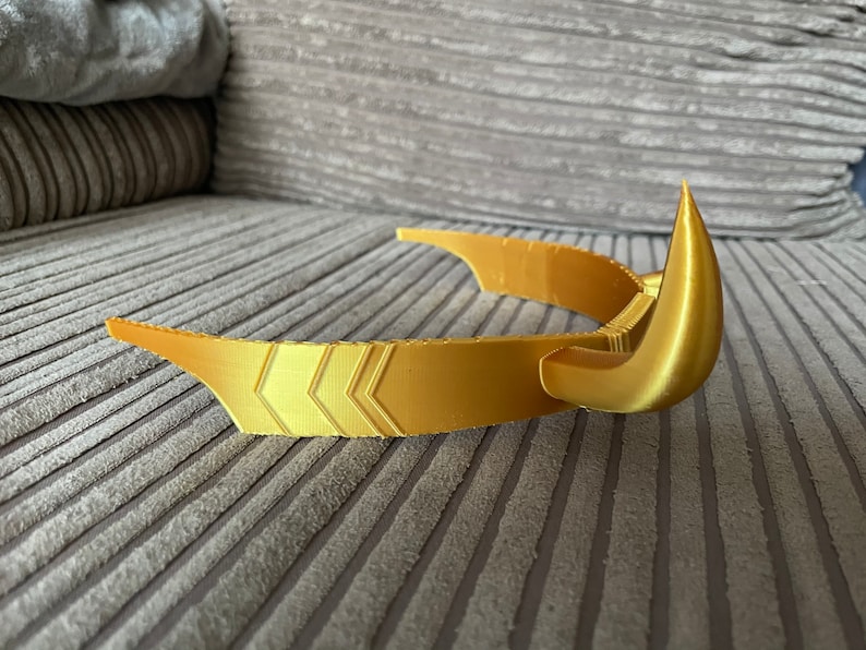 Puede incluir: Una corona dorada con un dise&ntilde;o curvo y puntas afiladas. La corona presenta patrones de chevr&oacute;n a lo largo de la banda. El dise&ntilde;o sugiere un tema de fantas&iacute;a o cosplay.