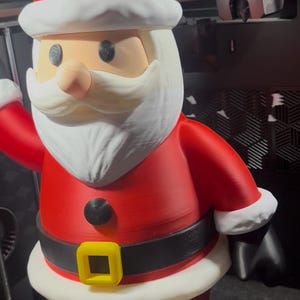 May include: A 3D-printed Santa Claus figure. The figure is wearing a red suit with a black belt and a yellow buckle. The hat is red with a white trim and a white pom-pom. The face is tan with a white beard and mustache.