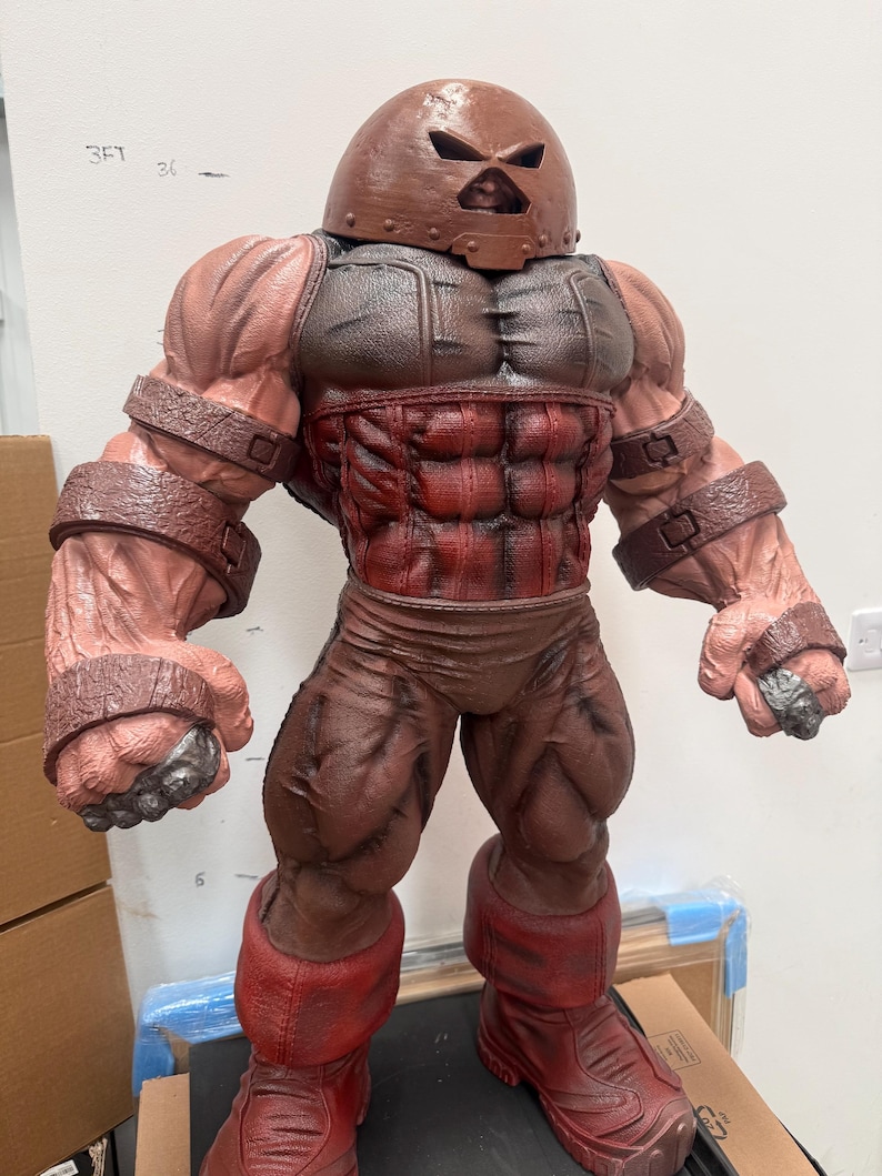 May include: A detailed figurine of the Juggernaut, a Marvel Comics character. The figure is predominantly brown and red, with a helmet, armored chest, and muscular physique. The figure is standing upright, showcasing its powerful build.