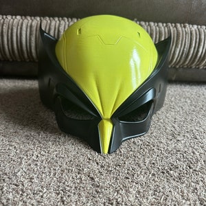 Pode incluir: Uma m&aacute;scara de pl&aacute;stico amarela e preta de um super-her&oacute;i com dentes e garras afiados. A m&aacute;scara tem um design detalhado com uma superf&iacute;cie texturizada.