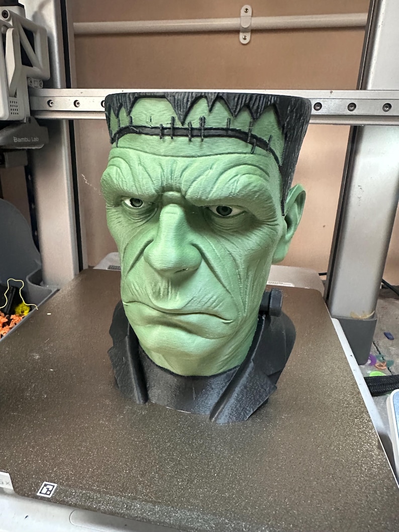 Puede incluir: Busto verde y negro del monstruo de Frankenstein. El busto tiene una cara verde con una expresi&oacute;n seria, cabello negro y una chaqueta negra. Es un art&iacute;culo decorativo.