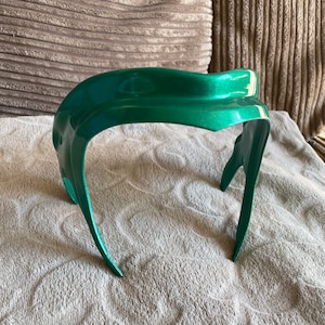 K&ouml;nnte beinhalten: Ein gr&uuml;nes Plastik-Haarband mit einem geschwungenen Design. Das Haarband ist aus glattem, gl&auml;nzendem Plastik.