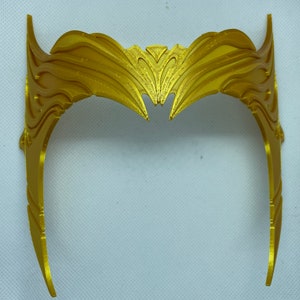 May include: A gold-coloured crown with a decorative, intricate design. The crown is made of a smooth, shiny material and has a pointed top.
