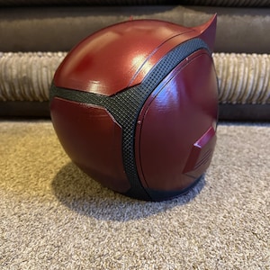 以下が含まれることがあります： 赤と黒のデアデビルヘルメットで、表面はテクスチャ加工されています。ヘルメットはプラスチック製で、洗練されたモダンなデザインです。