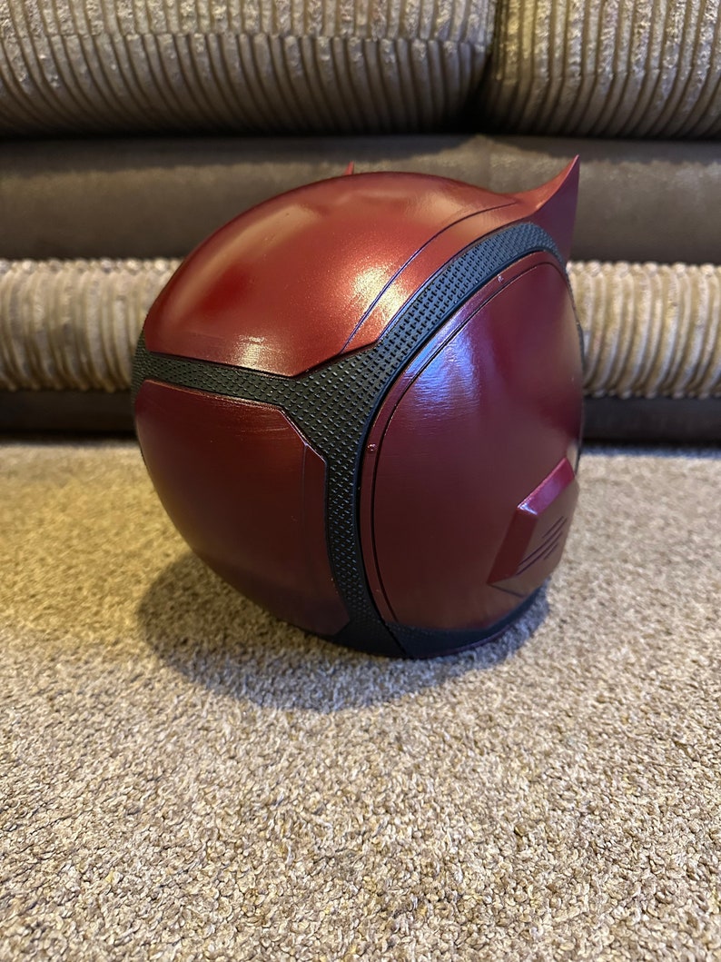 以下が含まれることがあります： 赤と黒のデアデビルヘルメットで、表面はテクスチャ加工されています。ヘルメットはプラスチック製で、洗練されたモダンなデザインです。
