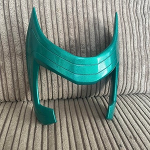 May include: A teal green plastic headband with a curved design. The headband is made of a smooth, shiny plastic.