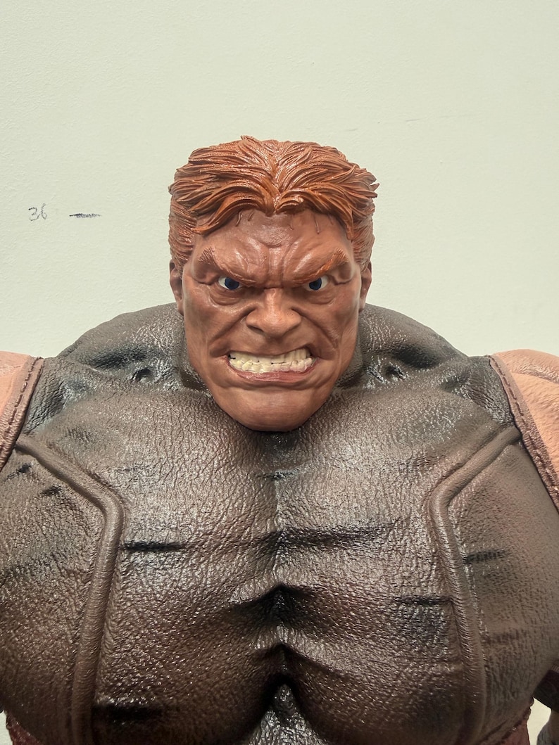 May include: A detailed action figure of a muscular character with a stern expression. The figure has red hair, a brown complexion, and is wearing a brown and tan outfit. The figure's face is contorted in an angry grimace.
