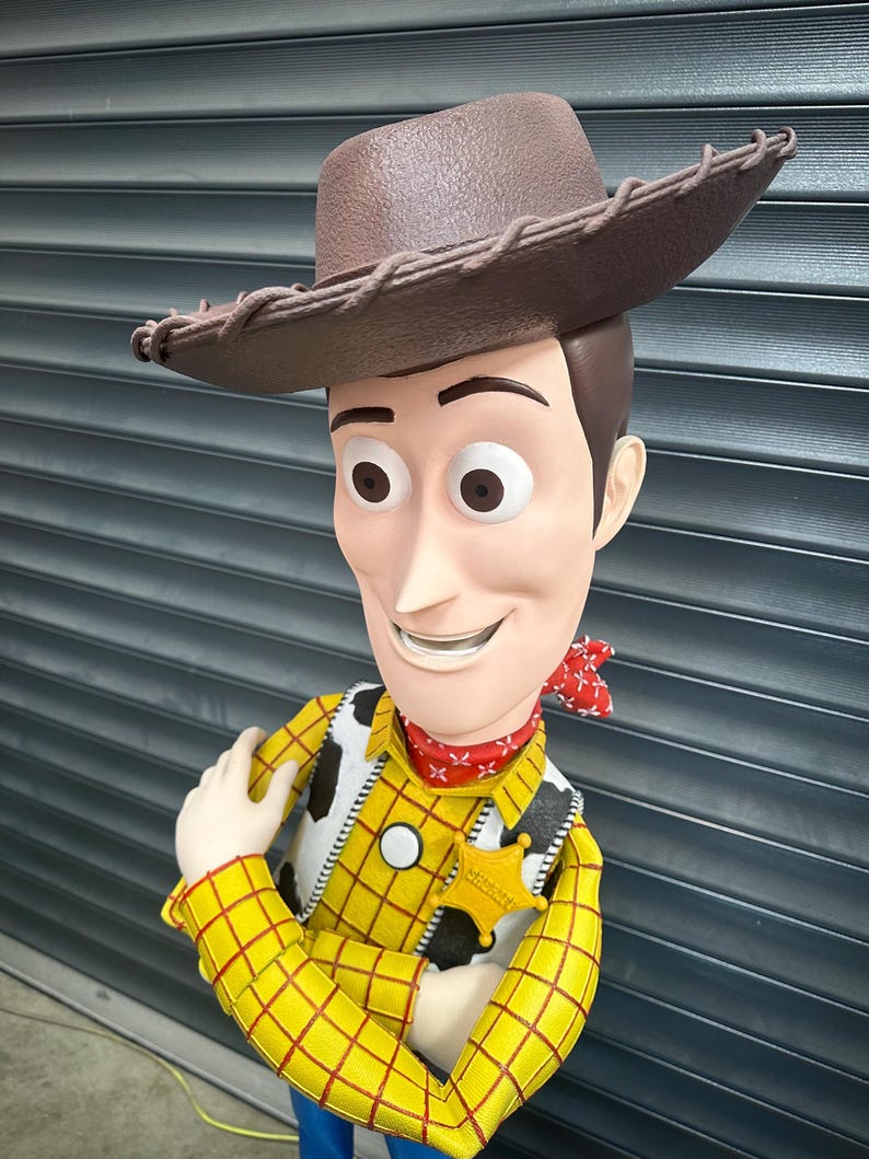 May include: A detailed figurine of Woody from Toy Story. The figure wears a brown cowboy hat, a yellow plaid shirt, a cow-print vest, a red bandana, and a sheriff's badge. The figure has a smiling expression.