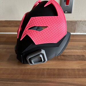May include: A black and pink plastic mask with a textured design. The mask has a gray detail on the side.