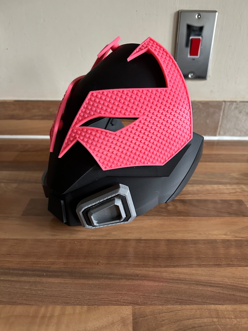May include: A black and pink plastic mask with a textured design. The mask has a gray detail on the side.