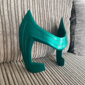 May include: A green plastic headband with a curved design. The headband is made of a smooth, shiny plastic and has a slightly textured surface.