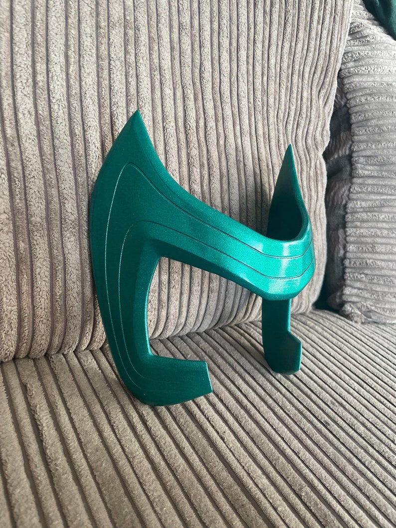 May include: A green plastic headband with a curved design. The headband is made of a smooth, shiny plastic and has a slightly textured surface.