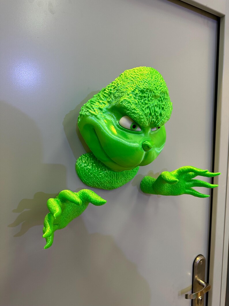 May include: A green Grinch character figurine with a mischievous expression, peeking around a door. The figurine is 3D printed and has a textured surface.