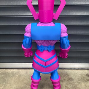 May include: A large, colorful action figure of Galactus, a fictional character. The figure is primarily pink and blue, with a detailed design. The figure has a helmet-like head and a muscular build, with a belt and boots. The figure is standing upright.