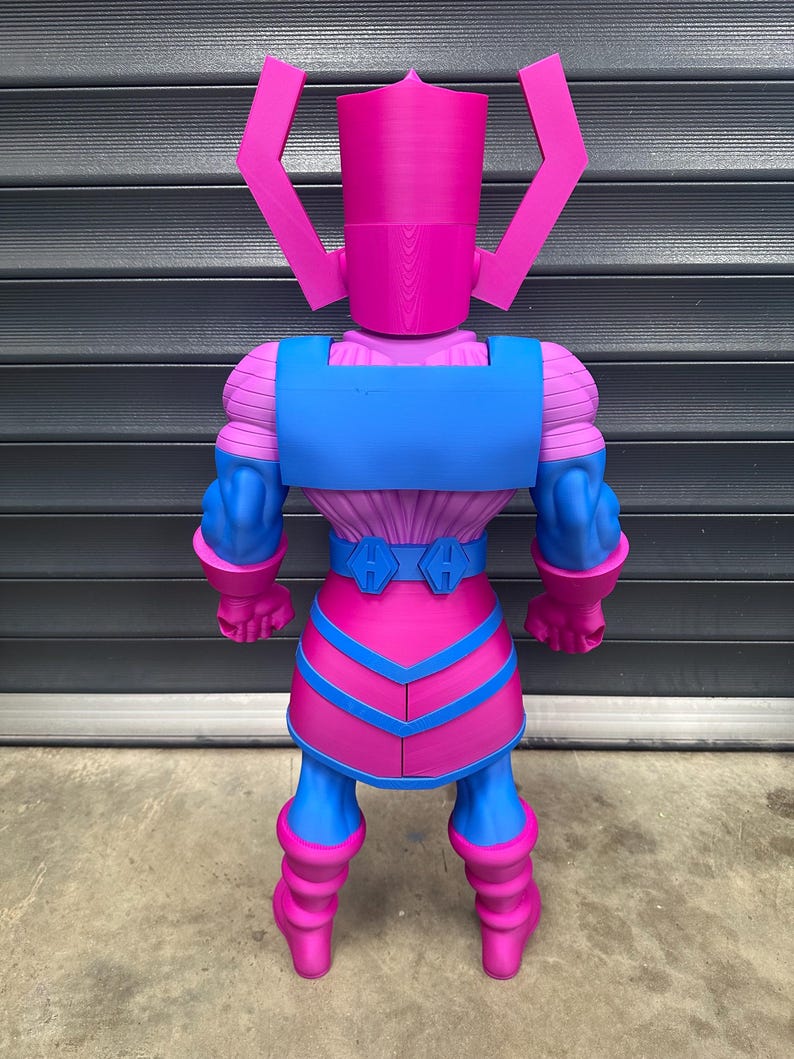 May include: A large, colorful action figure of Galactus, a fictional character. The figure is primarily pink and blue, with a detailed design. The figure has a helmet-like head and a muscular build, with a belt and boots. The figure is standing upright.
