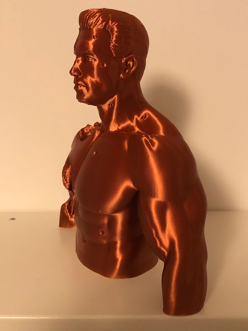 May include: A 3D printed bust of a muscular figure with a detailed face and torso. The bust is made of a copper-colored filament.