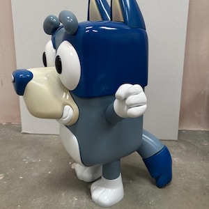 May include: A blue and gray cartoon wolf figurine with white eyes and a white mouth. The figurine is standing on a gray surface.