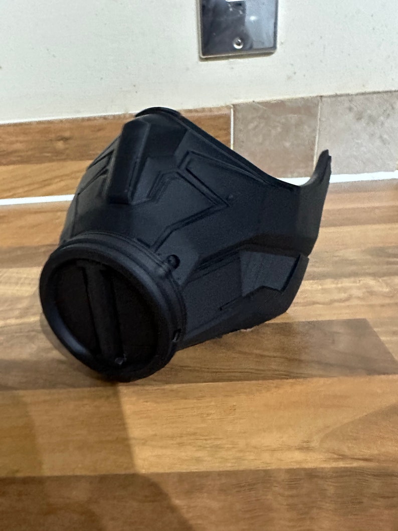May include: A black plastic mask with a geometric design. The mask has a large, round opening on the left side.