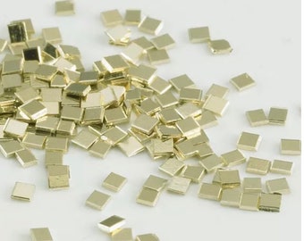 May include: A pile of small, square, gold-colored metal pieces. The pieces are scattered on a white surface.