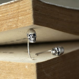 May include: Two silver skull bookends with a detailed design. The bookends are placed on a closed book.