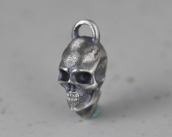 May include: A detailed, silver-colored skull pendant with a loop at the top for a chain. The skull has a textured surface and visible teeth. The pendant is a gothic-inspired accessory.