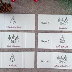 Pode incluir: Cart&otilde;es de Natal brancos com ilustra&ccedil;&otilde;es de &aacute;rvores pretas e texto em alem&atilde;o. Os cart&otilde;es s&atilde;o dobrados e apresentam sauda&ccedil;&otilde;es como "Sch&ouml;ne Weihnachtszeit" e "Frohe Weihnachten".