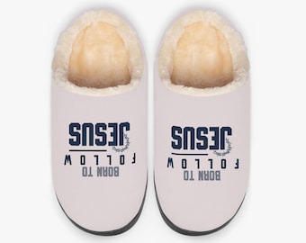 May include: A pair of light pink slippers with a cream-colored, fuzzy lining. The slippers have the words "JESUS" and "BORN TO FOLLOW" printed on them in navy blue and gray.