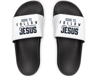 May include: Pair of black and white slide sandals. The white strap features the text "BORN TO FOLLOW JESUS" in navy blue. The sandals have a textured footbed.