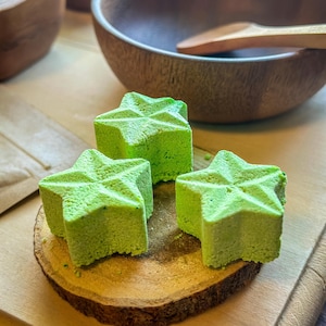 May include: Three green star-shaped bath bombs on a wooden surface. The bath bombs have a speckled texture.