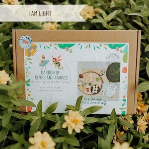 May include: A brown cardboard box with a white label that says "Garden of Elves and Fairies" and "Nature Inspired Mindful Potions". The box is open and shows a variety of items, including a wooden tray, a small green plant, and a small bottle of liquid. The label also says "A potion to make your own light shine" and "Created with natural ingredients".