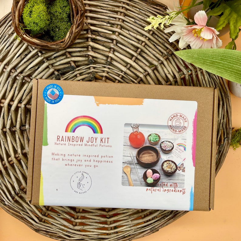 Puede incluir: Una caja de cart&oacute;n con un dise&ntilde;o de arco&iacute;ris y el texto "Rainbow Joy Kit" en la parte delantera. La caja contiene un conjunto de ingredientes naturales para hacer pociones conscientes. El texto "Made in USA" est&aacute; en la caja.