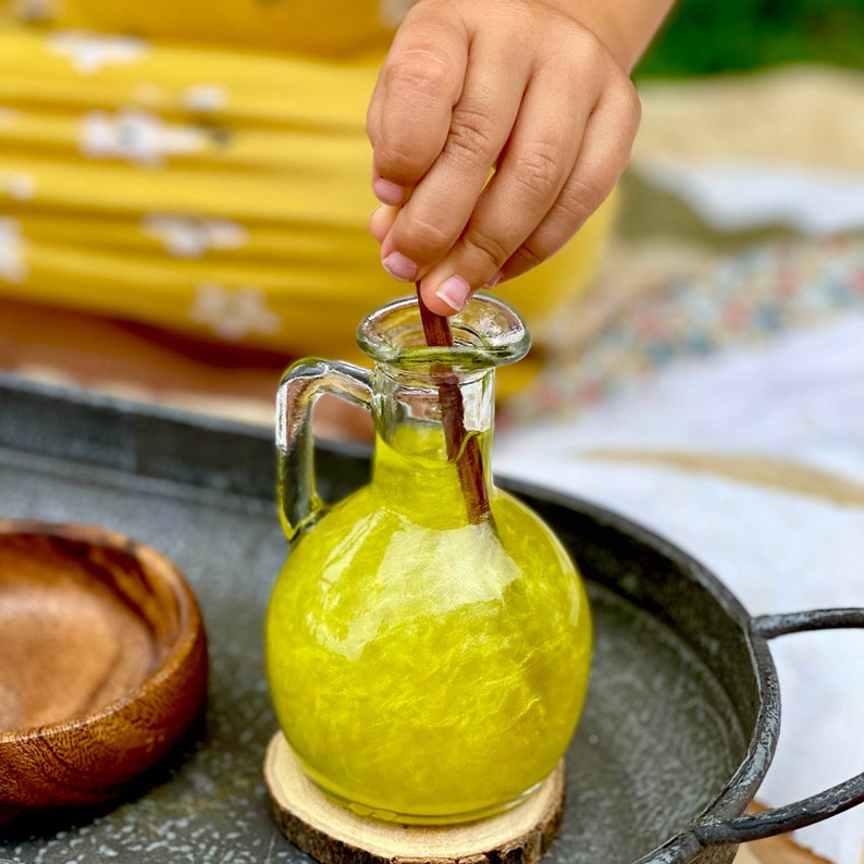 May include: A clear glass bottle with a yellow liquid inside. The bottle has a textured surface and a wooden stick is inserted into the liquid.