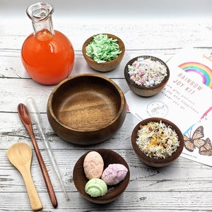 Puede incluir: Un kit de alegr&iacute;a arco&iacute;ris con una variedad de bombas de ba&ntilde;o coloridas, sales de ba&ntilde;o y otros productos de ba&ntilde;o. El kit incluye una botella de vidrio con l&iacute;quido naranja, cuencos de madera y una cuchara de madera. El kit est&aacute; etiquetado como "Rainbow Joy Kit" e incluye el texto "Nuestras pociones de juego traen alegr&iacute;a y felicidad dondequiera que vayas."