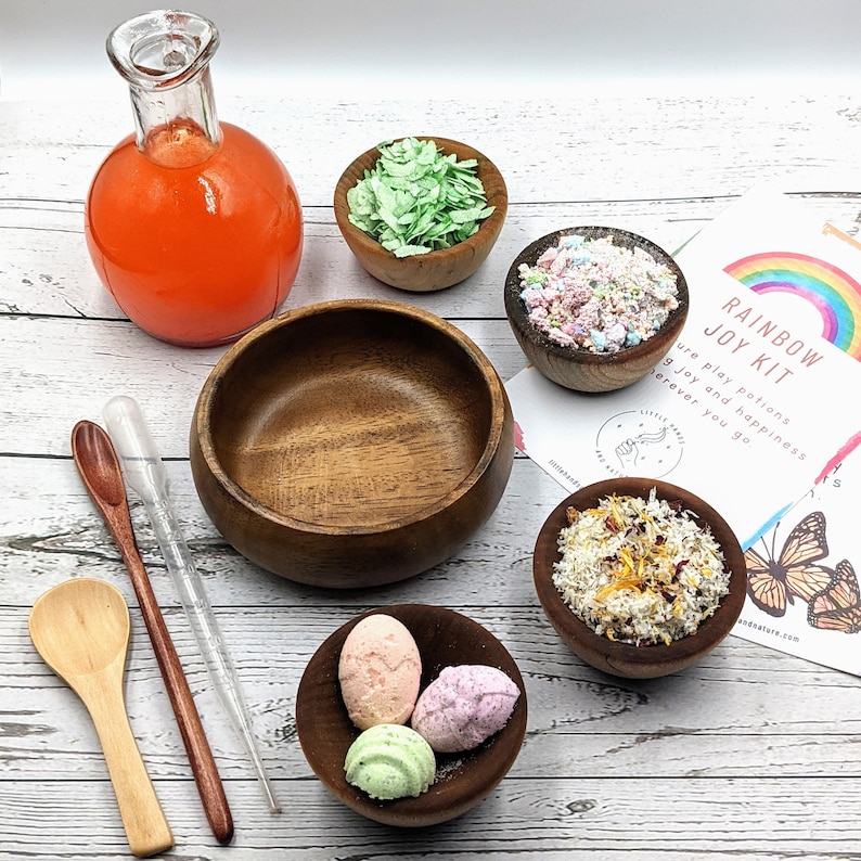 Puede incluir: Un kit de alegr&iacute;a arco&iacute;ris con una variedad de bombas de ba&ntilde;o coloridas, sales de ba&ntilde;o y otros productos de ba&ntilde;o. El kit incluye una botella de vidrio con l&iacute;quido naranja, cuencos de madera y una cuchara de madera. El kit est&aacute; etiquetado como "Rainbow Joy Kit" e incluye el texto "Nuestras pociones de juego traen alegr&iacute;a y felicidad dondequiera que vayas."