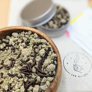 May include: A wooden bowl filled with a mixture of light green and brown sprinkles. The sprinkles are a combination of small, crumbly pieces and long, thin chocolate pieces.
