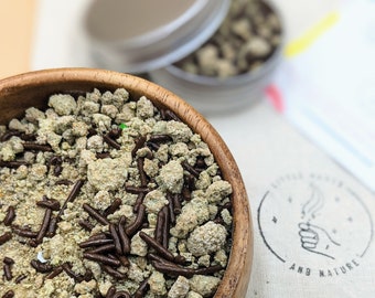 May include: A wooden bowl filled with a mixture of light green and brown sprinkles. The sprinkles are a combination of small, crumbly pieces and long, thin chocolate pieces.