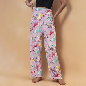 May include: Light purple pajama pants with a repeating pattern of unicorns, rainbows, stars, and hearts. The pants have a soft, fuzzy texture and a wide-leg design. The colors include pink, blue, yellow, and red.