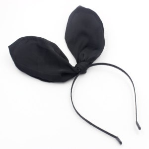 May include: Black fabric bunny ear headband. The headband is made of a thin black elastic band with two black fabric ears attached to the top.