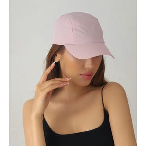 May include: A light pink baseball cap with a curved brim. The cap is made of a lightweight material and has a classic six-panel design. The cap is a solid color and is suitable for outdoor activities.