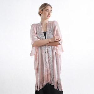 May include: A light pink, open-front kimono-style cover-up with silver sequin embellishments. The cover-up has short sleeves and a fringe hem. The model is wearing a black top and black skirt.