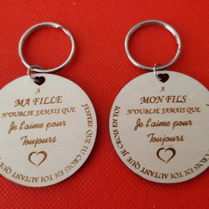 Pode incluir: Dois chaveiros redondos com argolas prateadas. Cada chaveiro é gravado com texto em francês e um símbolo de coração. O texto inclui frases como "Eu te amo para sempre" e "Minha filha/filho".