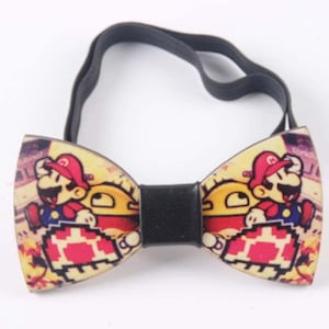 Puede incluir: Una pajarita de madera con una correa elástica negra ajustable. La pajarita presenta una impresión colorida de un personaje de videojuego.