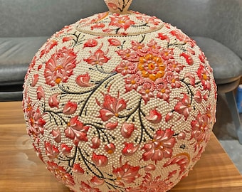 May include: A white ceramic lamp with a floral design in shades of pink, red, and orange. The lamp has a round base and a pointed top. The lamp is decorated with small white beads.