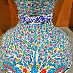 May include: A large, blue and white ceramic vase with a floral pattern. The vase has a wide base and a narrow neck. The floral pattern is intricate and detailed, and it features red, white, and green flowers.