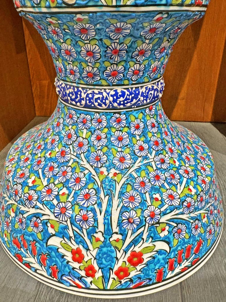 May include: A large, blue and white ceramic vase with a floral pattern. The vase has a wide base and a narrow neck. The floral pattern is intricate and detailed, and it features red, white, and green flowers.