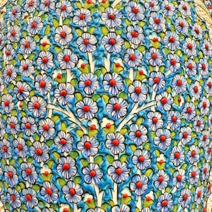 May include: A close-up of a ceramic vase with a blue and white floral pattern. The vase is covered in small, white flowers with red centers. The flowers are arranged in a repeating pattern.